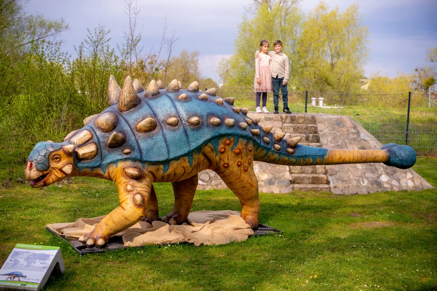 Blick auf einen Dinosaurier der Dino-Ausstellung im Elbauenpark. Im Hintergrund zwei Kinder.
