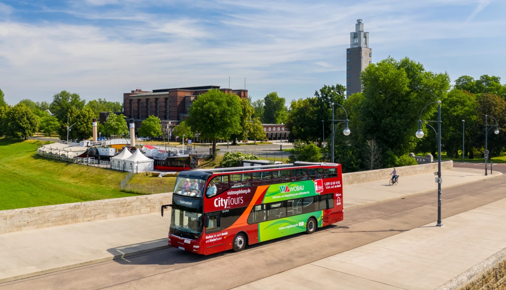 Der rote CityTours-Doppeldeckerbus mit offenem Oberdeck faehrt ueber die Strombruecke, dahinter Stadthalle und Albinmueller-Turm im Stadtpark