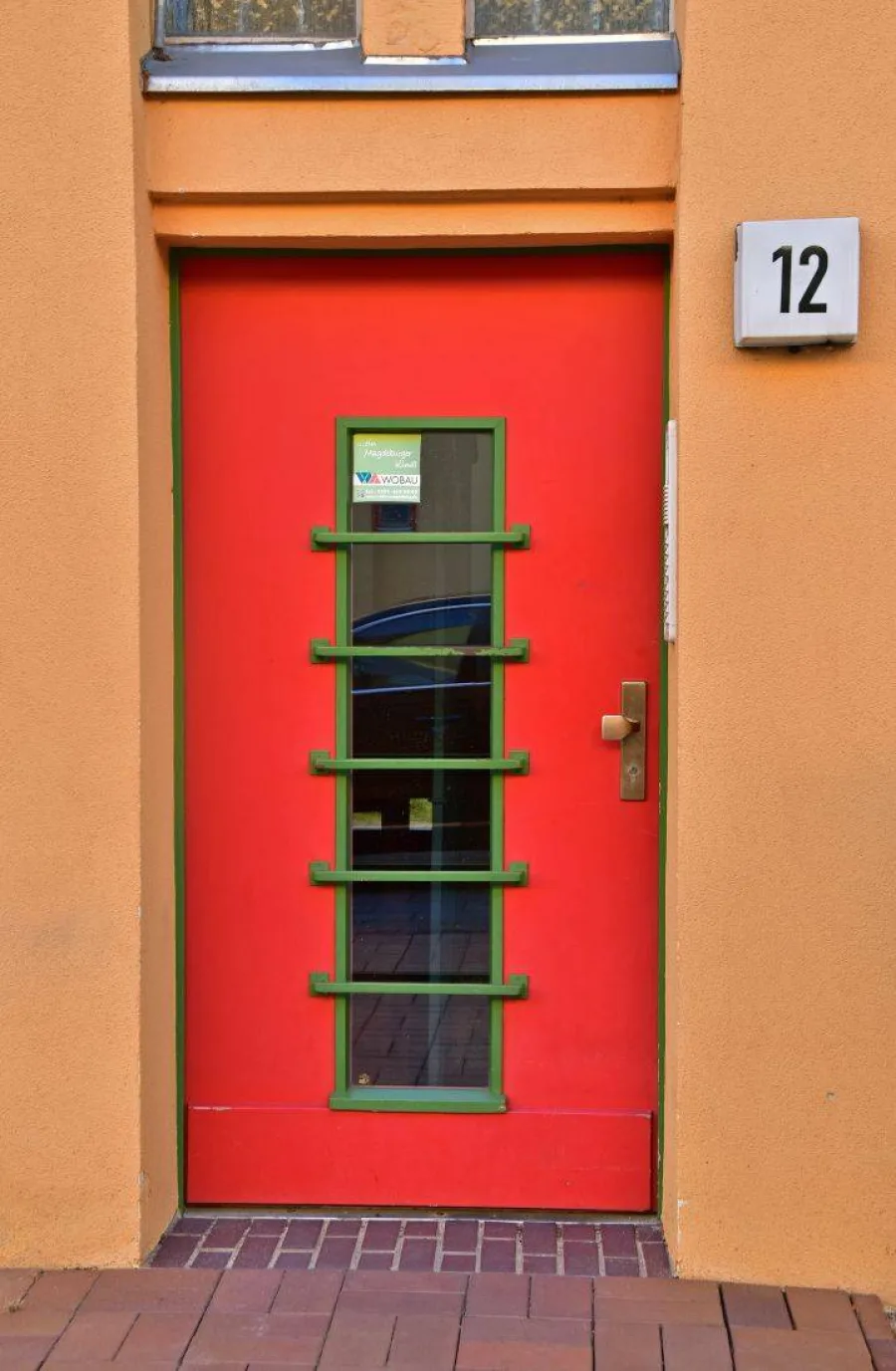 Rote Haust&uuml;r mit gr&uuml;nen Sprossen und der Hausnummer 12 an einer ockerfarbenen Fassade der Beimssiedlung