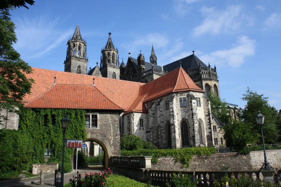 Der Dom von Sueden mit dem efeuberankten Remtergang-Tor: rote Ziegeldaecher der Klausurgebaeude, dahinter Chor und Tuerme unter blauem Himmel