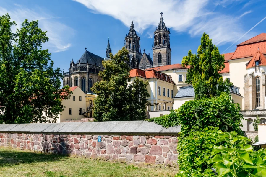 Blick ueber die rote Bruchsteinmauer am Fuerstenwall auf Dom und Domklausur mit ihren roten Daechern unter blauem Sommerhimmel