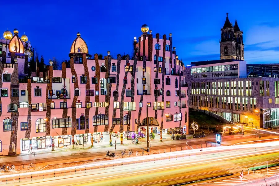 Die rosa Fassade der Gruenen Zitadelle zur blauen Stunde, rechts der beleuchtete Domturm, davor Lichtspuren des Verkehrs auf dem Breiten Weg