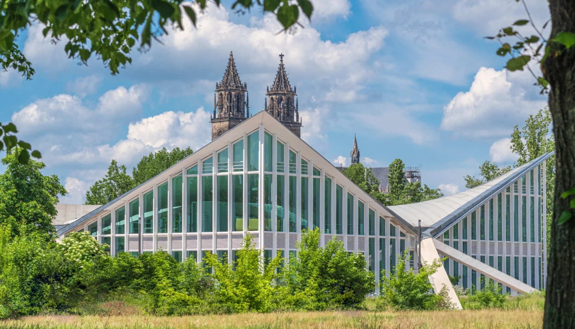 Die sanierte Hyparschale mit ihren geschwungenen Glasfassaden im Rotehornpark, dahinter die Tuerme des Magdeburger Doms