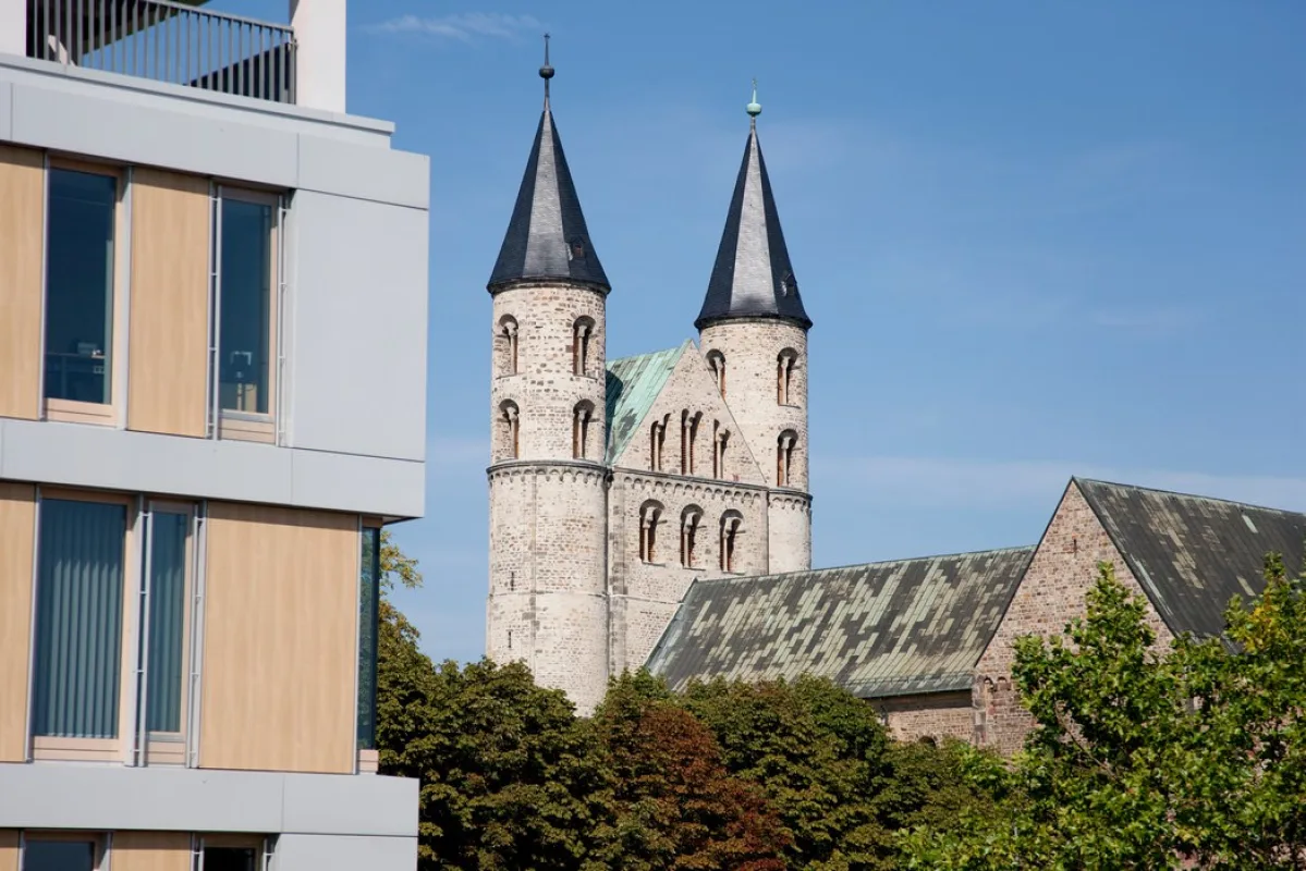 Die beiden spitzen T&uuml;rme der Klosterkirche Unser Lieben Frauen &uuml;ber Baumkronen, davor die helle Fassade eines modernen B&uuml;rohauses