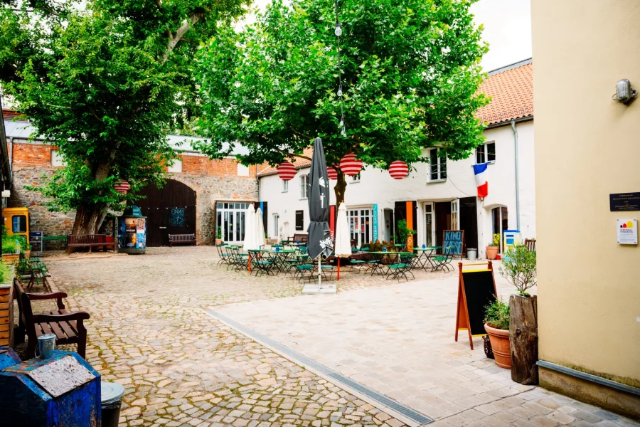 Gepflasterter Innenhof des Moritzhofs mit Sonnenschirmen, gelber B&uuml;cherzelle und franz&ouml;sischer Flagge am Eingang des Kinos