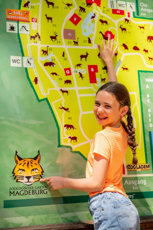 M&auml;dchen zeigt lachend auf den &Uuml;bersichtsplan des Zoologischen Gartens Magdeburg